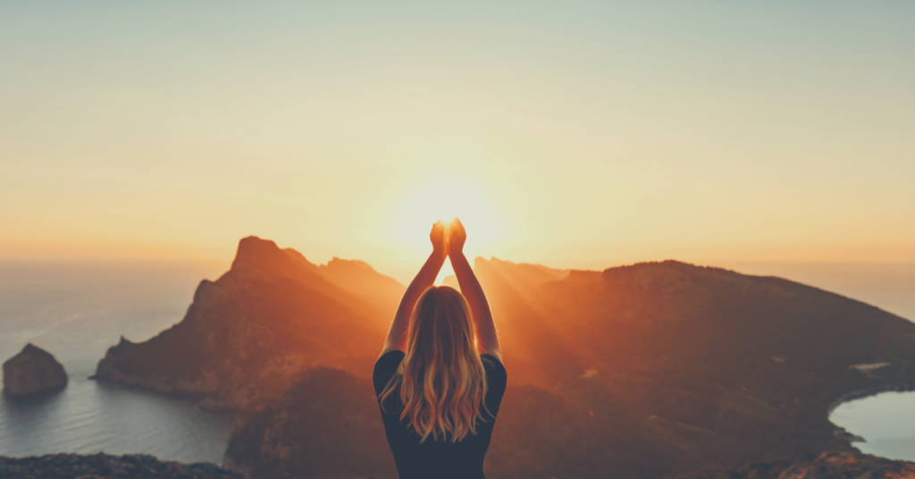 A woman on a mountain holding her hands up toward the sky